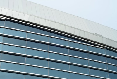 A modern architectural structure featuring a facade with large reflective windows and sleek metal paneling. The building has a curving roofline and the windows incorporate dark tinted glass, offering a sleek and contemporary appearance.