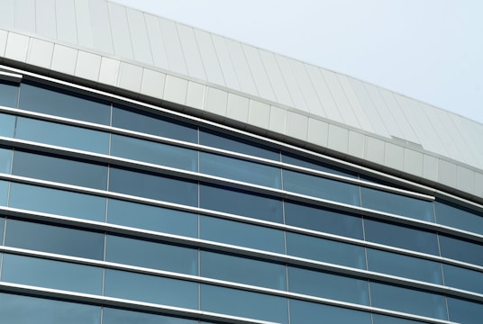 A modern architectural structure featuring a facade with large reflective windows and sleek metal paneling. The building has a curving roofline and the windows incorporate dark tinted glass, offering a sleek and contemporary appearance.
