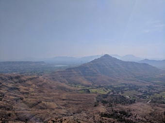 A scenic landscape showcasing a vast expanse of hilly terrain with scattered vegetation. A series of wind turbines is visible on the hilltops, emphasizing the presence of renewable energy infrastructure. The sky is clear, with a gentle haze in the distance, adding depth to the visual.