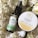 A flat lay composition showcases a dark glass bottle labeled 'Pharma Hemp' and a round container labeled 'Ginger Honey Hemp Body Balm,' surrounded by white flowers with green stems. The bottle appears to be a form of hemp oil, while the circular container is likely a skincare product.