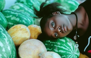 woman wearing black and white shirt leaning head on green watermelon fruits near cantaloupe