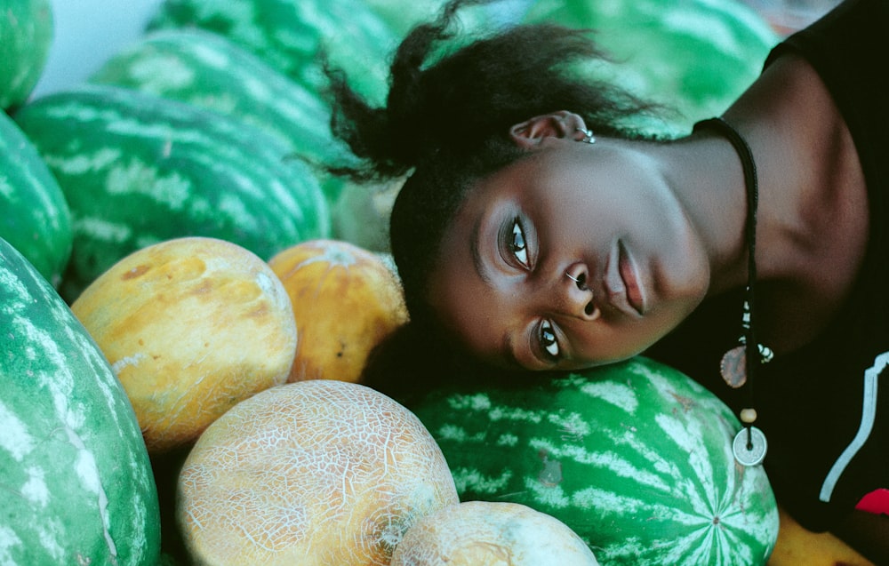 woman wearing black and white shirt leaning head on green watermelon fruits near cantaloupe