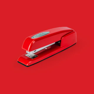 A sleek red stapler resting on a clean white desk, with a subtle crimson background.