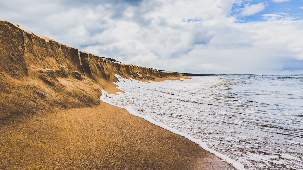 areia marrom ao lado do corpo de água durante o dia