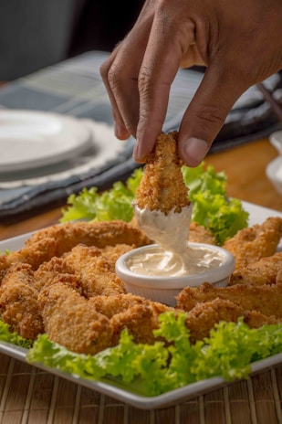 Close-up of a hand dipping a crispy chicken tender into a creamy sauce at Dave's Hot Chicken.