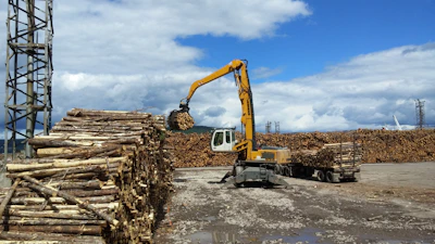 Industrial machinery loading timber logs onto transport trucks.