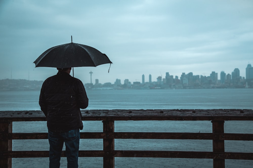 man using umbrella standing on wooden dock