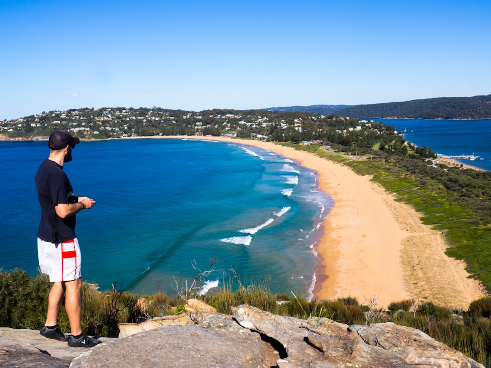 woman standing on rock formation looking at beach