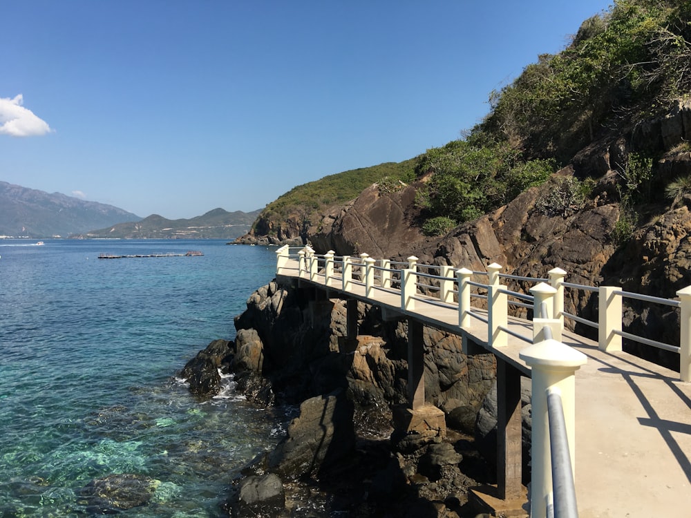 Weiße Beton-Minibrücke in der Nähe von felsigen Klippen mit Blick auf das Meer unter blauem und weißem Himmel