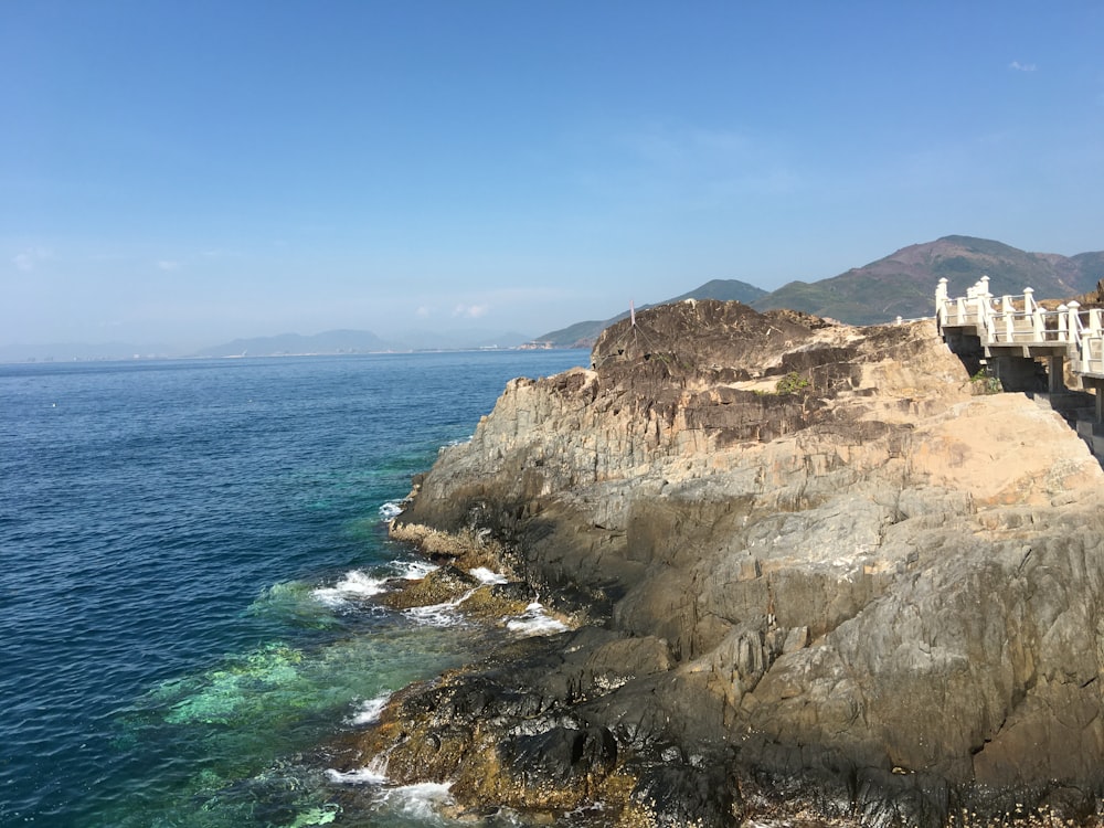 rocky hill viewing blue sea under blue and white skies