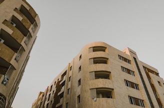 High-rise residential buildings with modern architectural design. The structures feature multiple floors with balconies and windows. The facade is composed of neutral-colored materials, giving it a sleek and sophisticated look.