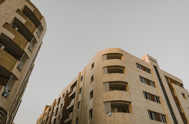High-rise residential buildings with modern architectural design. The structures feature multiple floors with balconies and windows. The facade is composed of neutral-colored materials, giving it a sleek and sophisticated look.