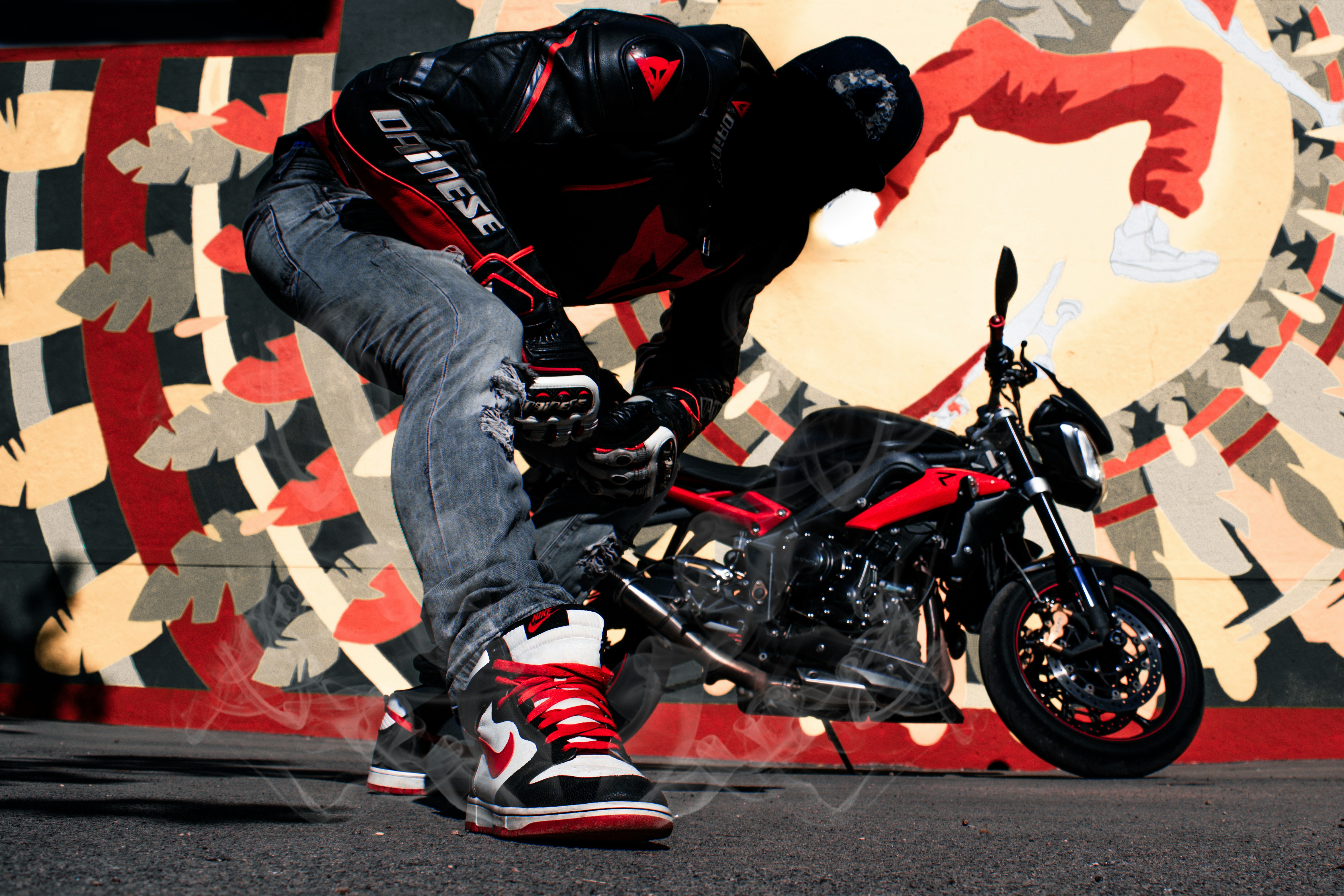 homme portant une veste en cuir noir et rouge à côté d’une moto nue