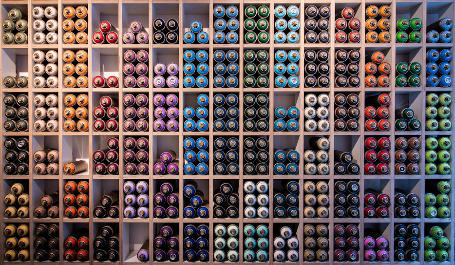 A vibrant display of colorful Asian Paints cans neatly arranged on wooden shelves in a cozy Madurai shop.