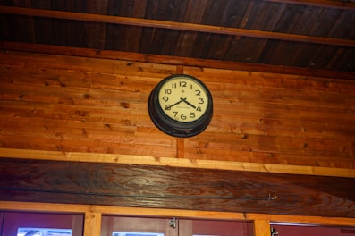 A warm wooden wall clock with natural grain, mounted in a cozy beige room.