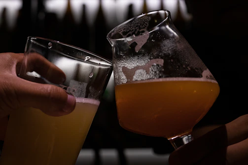 Close-up of a couple clinking glasses of amber craft beer in a warm rustic setting.
