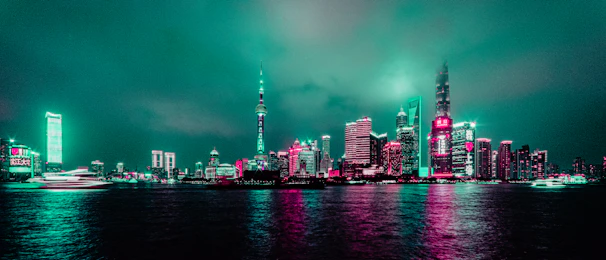 A vibrant cityscape at dusk with sleek modern architecture illuminated by teal and white lights.