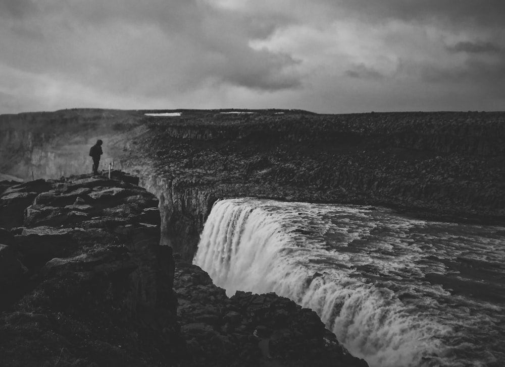 grayscale photo of person standing on cliff