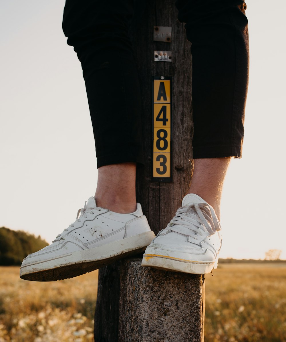 person wearing black pants and white low-top shoes sitting on post