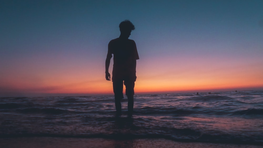 man standing at beach during sunset