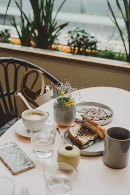 A cozy café table with a steaming cup of espresso, a fresh fruit juice, and a natural sandwich artfully arranged.
