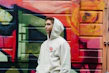 Close-up of a black hoodie with bold red graffiti-style logo on the chest, hanging against a cracked concrete wall.