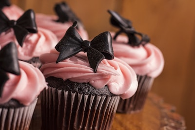 Elegant cupcakes with black wrappers topped with soft pink buttercream and tiny edible pearls.