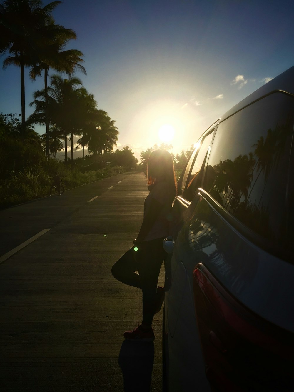 woman wearing shirt and black pants leaning on white vehicle