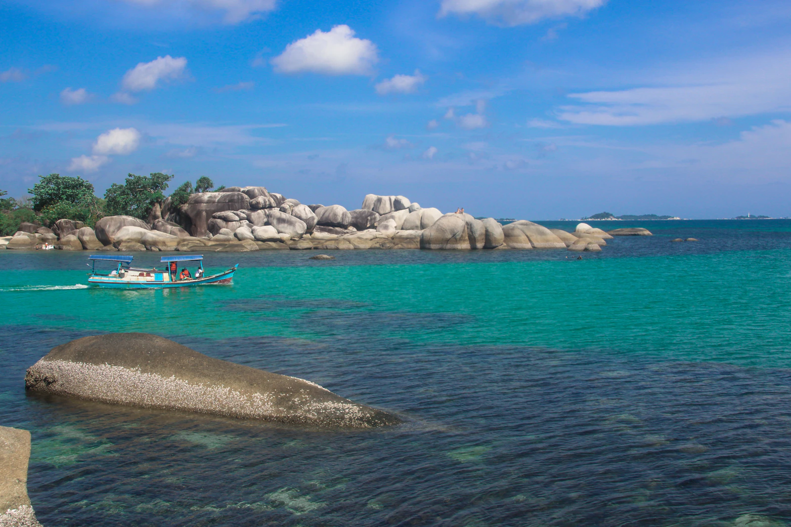 Perahu di atas air laut tenang bergradasi toska di Belitung