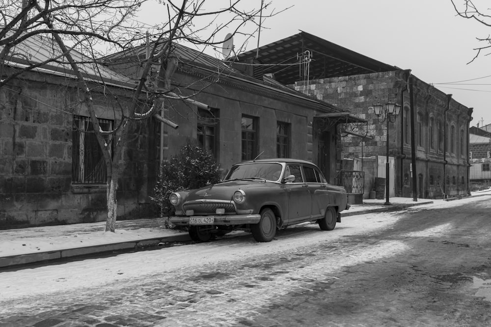 Une photo en noir et blanc d’une vieille voiture garée dans une rue enneigée
