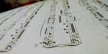 A close-up view of a sheet of musical notation featuring various notes, clefs, and musical symbols laid out on a staff. The image focuses on the details of the music manuscript with emphasis on the notes and lines.