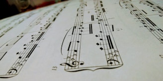 A close-up view of a sheet of musical notation featuring various notes, clefs, and musical symbols laid out on a staff. The image focuses on the details of the music manuscript with emphasis on the notes and lines.