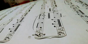 Close-up of a handwritten instrumental sheet music spread across a wooden desk with scattered pencils.