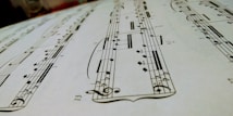 A close-up view of a sheet of musical notation featuring various notes, clefs, and musical symbols laid out on a staff. The image focuses on the details of the music manuscript with emphasis on the notes and lines.