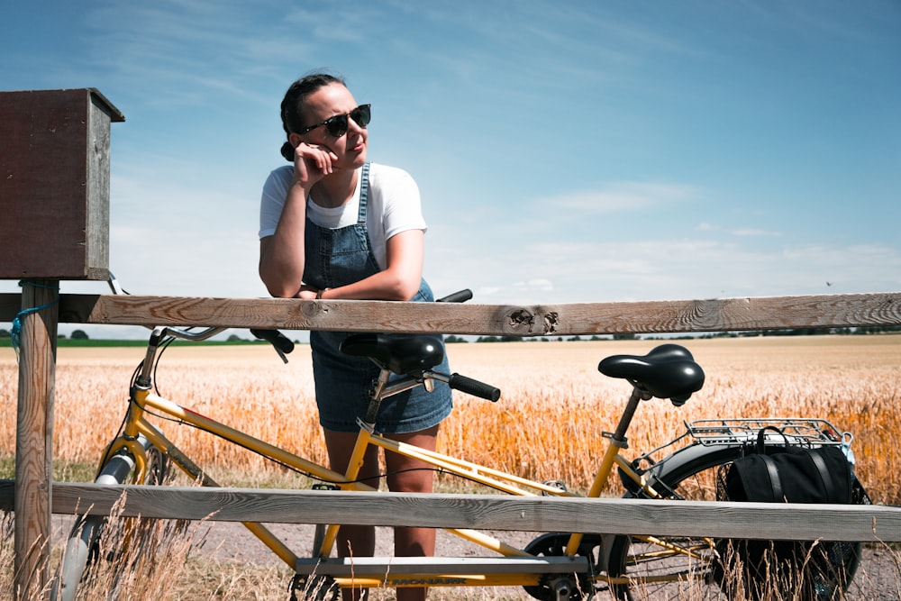 woman leaning on wooden fence near tandem bike at the grassfield
