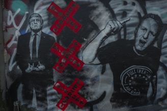 Graffiti artwork featuring two figures, one in a suit and the other with an expressive hand gesture. The background includes red Xs with the word 'CORRUPT' in black. Various colors and textures are visible, adding depth and complexity.