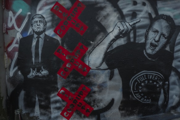 Graffiti artwork featuring two figures, one in a suit and the other with an expressive hand gesture. The background includes red Xs with the word 'CORRUPT' in black. Various colors and textures are visible, adding depth and complexity.