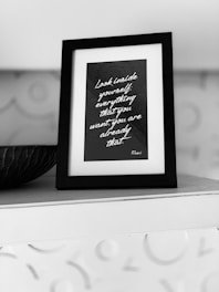 A black and white framed quote on a shelf, surrounded by a textured background. The quote reads, 'Look inside yourself; everything that you want, you are already that.' Attributed to Rumi, the text is written in a script font on a dark background.