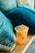A refreshing drink with slices of lemon and lime in a clear plastic cup sits on a wooden table. The setting includes textured turquoise pillows, suggesting a casual and cozy environment.
