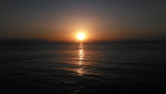 A warm sunset over a calm ocean with a silhouette of a traveler looking at the horizon.