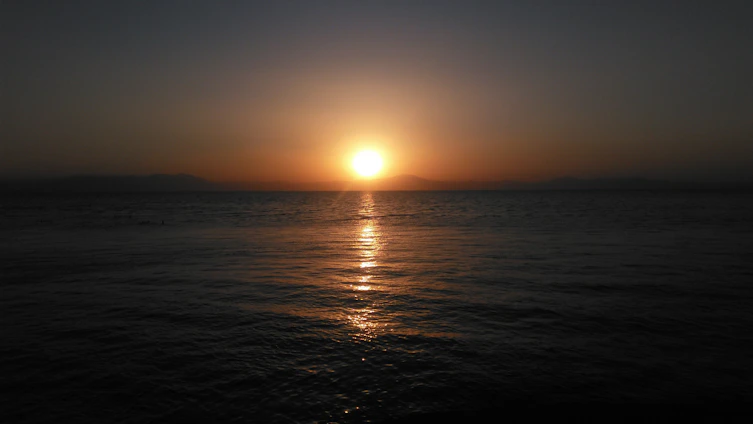 A warm sunset over a calm ocean, with a silhouette of a traveler gazing at the horizon.
