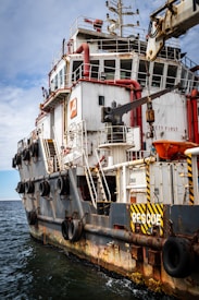 A large rescue ship on the water is visible, featuring a robust structure with multiple decks and safety equipment on board. The hull is painted with a combination of white and dark colors, and there are several large tires attached to the side, presumably for protection or docking purposes. Red pipes and lifebuoys are mounted on the exterior, and the words 'RESCUE' and 'SAFETY FIRST' are prominently displayed. The ship is equipped with cranes and other machinery, indicating its readiness for emergency situations.