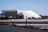 Several large white pyramidal mounds stand near industrial buildings under a clear blue sky. The area appears to be a salt processing facility, with noticeable mounds of salt and construction equipment scattered around.