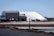 Several large white pyramidal mounds stand near industrial buildings under a clear blue sky. The area appears to be a salt processing facility, with noticeable mounds of salt and construction equipment scattered around.