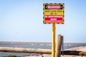A warning sign is prominently displayed, attached to a yellow post with a chain. The sign indicates a mine lease area, ML 37, with a message that no unauthorized entry is allowed and trespassers will be prosecuted. The sign is red and yellow with black stripes, positioned in an open, natural landscape with blue sky above.