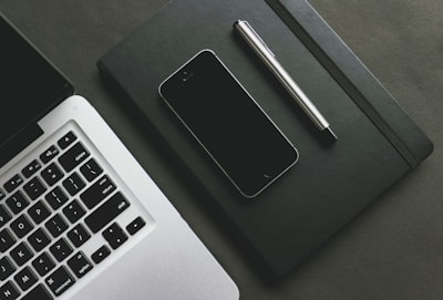 A close-up of hands typing on a laptop, surrounded by tech gadgets and a notepad.