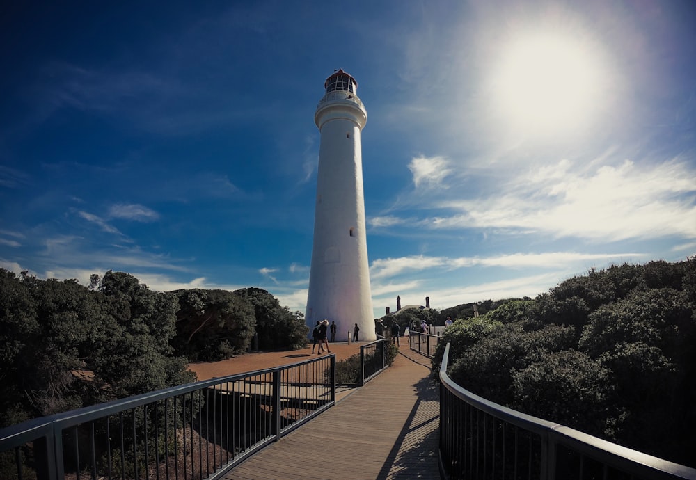 white and red lighthouse beside brown and gray bridge