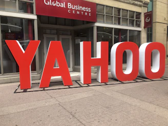Large red and white letters spelling out 'YAHOO' are positioned outside a building labeled 'Global Business Centre.' The letters are three-dimensional and stand on the sidewalk, creating a striking visual against the building's facade.