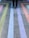 A person stands on a concrete surface with colorful stripes arranged in a geometric pattern. The stripes include shades of green, blue, purple, and orange, creating a vibrant visual effect.