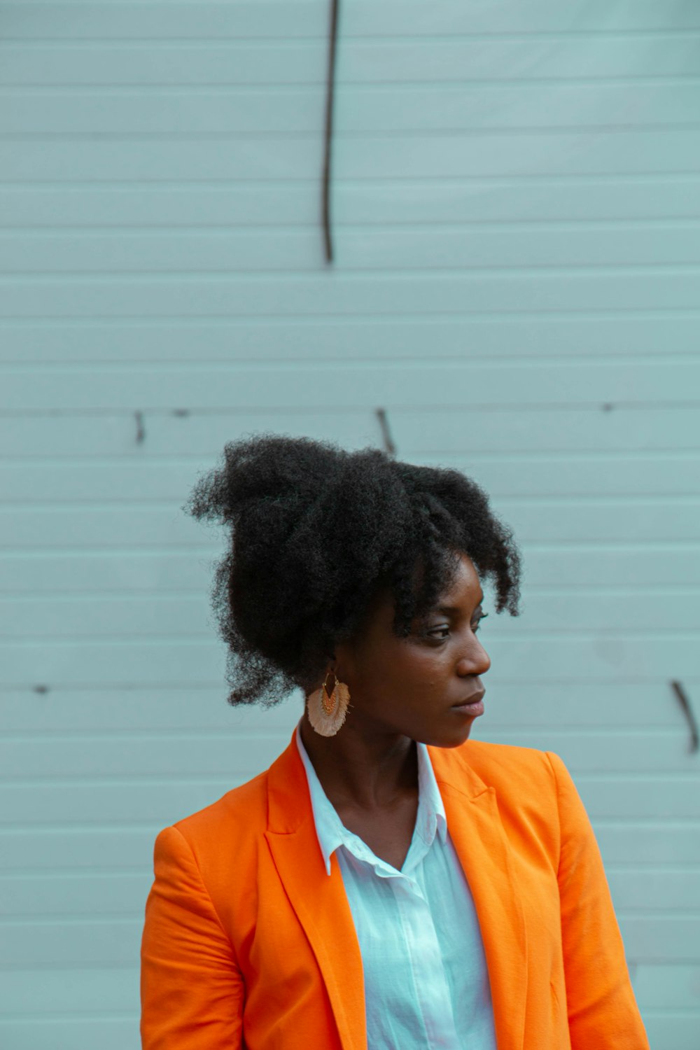 Mujer con blazer naranja de pie cerca de la pared blanca